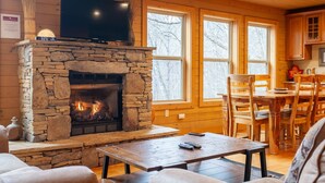 A cozy cabin interior with a stone fireplace, wooden walls, and large windows. - Almond Joy Hideaway Luxury cabin, fire pit, Bryson City, Fontana Lake (Almond)