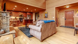 A cozy cabin interior with a stone fireplace, wooden ceiling, a sofa, and a kitchen area. - Almond Joy Hideaway Luxury cabin, fire pit, Bryson City, Fontana Lake (Almond)