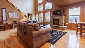 A cozy cabin interior with a stone fireplace, wooden walls, and large windows. - Almond Joy Hideaway Luxury cabin, fire pit, Bryson City, Fontana Lake (Almond)