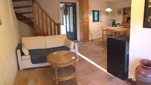 Una sala de estar con un sofá, una mesita redonda, un mueble negro y una escalera que lleva a otra habitación.