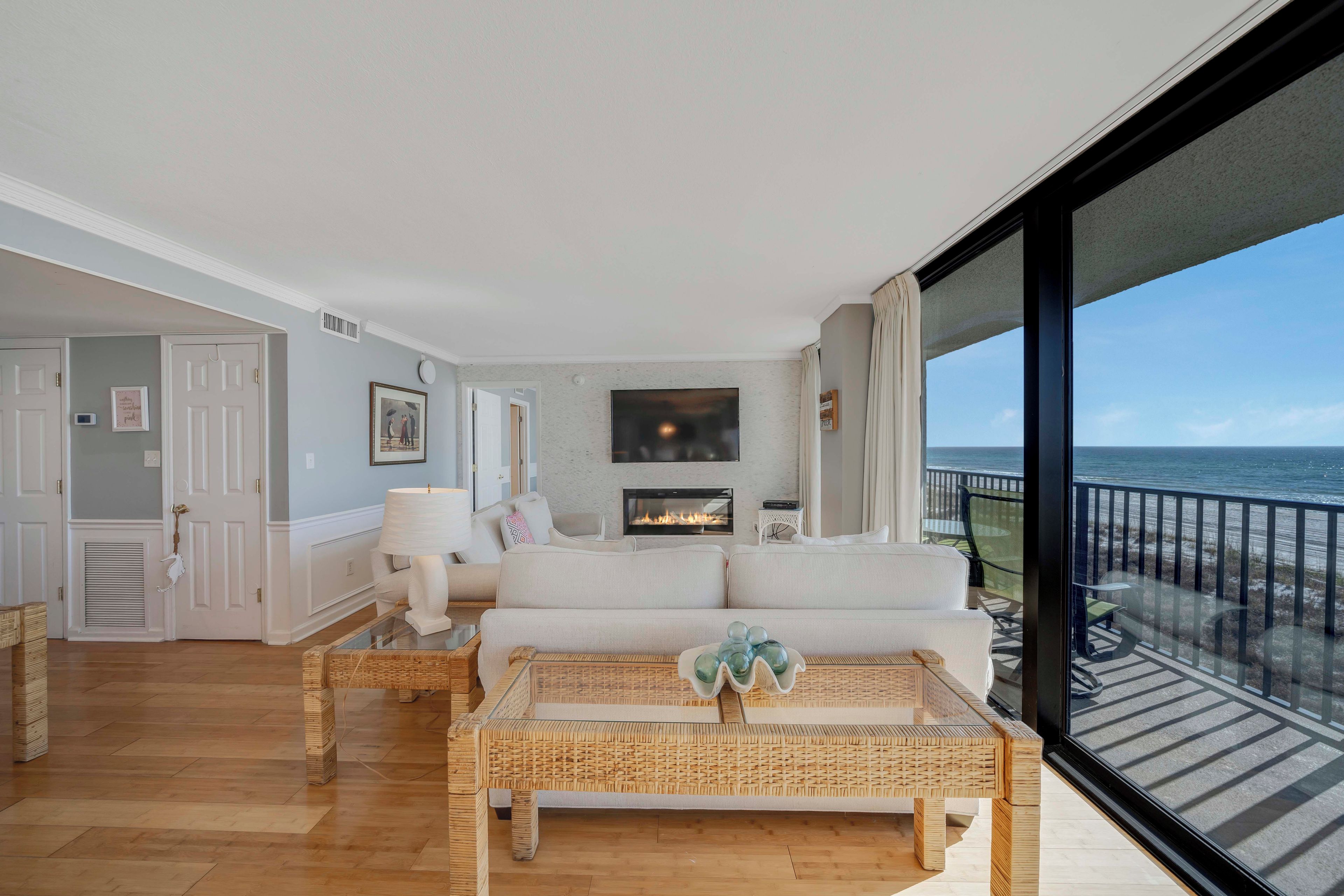 A modern living room with a fireplace, a sofa, a coffee table, and a view of the ocean through large windows.