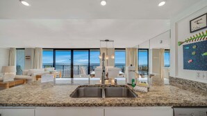 A modern kitchen with a granite countertop, stainless steel sink, and a dining area with a view of the ocean.