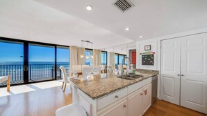 A modern kitchen with a large island, white cabinetry, and a view of the ocean.