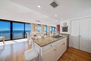 A modern kitchen with a large island, white cabinetry, and a view of the ocean.