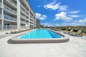 A swimming pool with lounge chairs, a building with balconies, and a clear sky. - Beachfront Mariner West 203 FREE Golf&Perks! Gulf Front Pool, Tennis & Grill! (Panama City Beach)