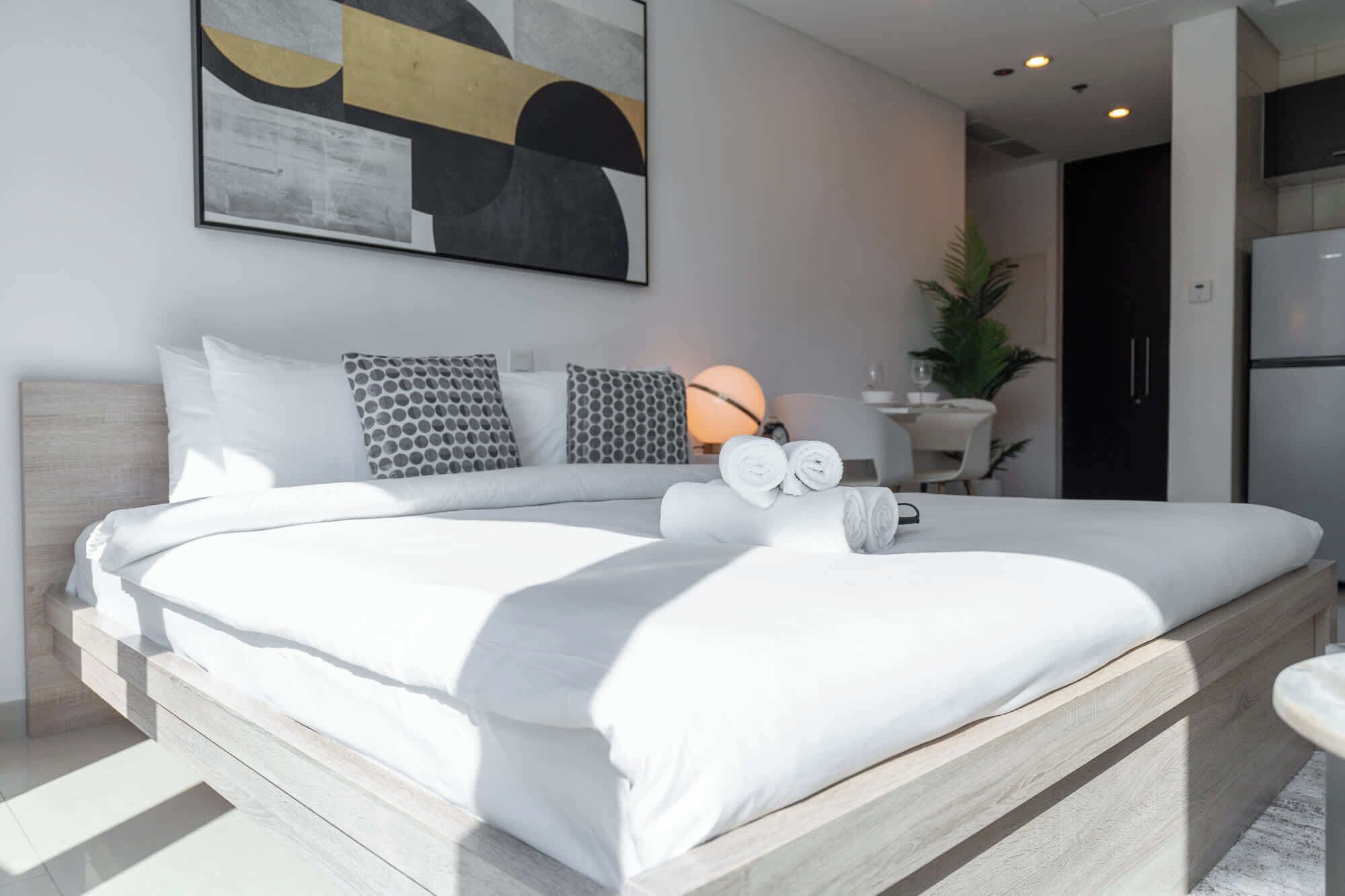 Un dormitorio moderno con una cama grande, un cuadro abstracto en la pared, una lámpara de noche y una mesita con una planta.