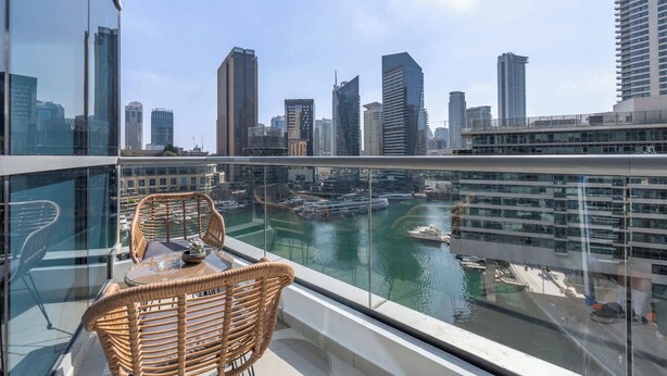 A balcony with wicker furniture overlooking a marina and city skyline.