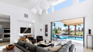 A modern living room with a grey sofa, a flat-screen TV, and a pool view.
