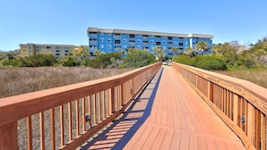 Une promenade en bois mène à un bâtiment bleu à étages, doté de plusieurs balcons.