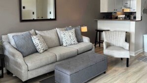 Un salon comprenant un canapé, un pouf, un fauteuil et un grand miroir accroché au mur.