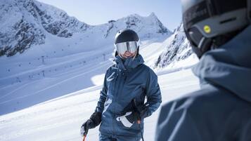 Una persona con tuta da sci blu e casco su una pista innevata, con montagne sullo sfondo.