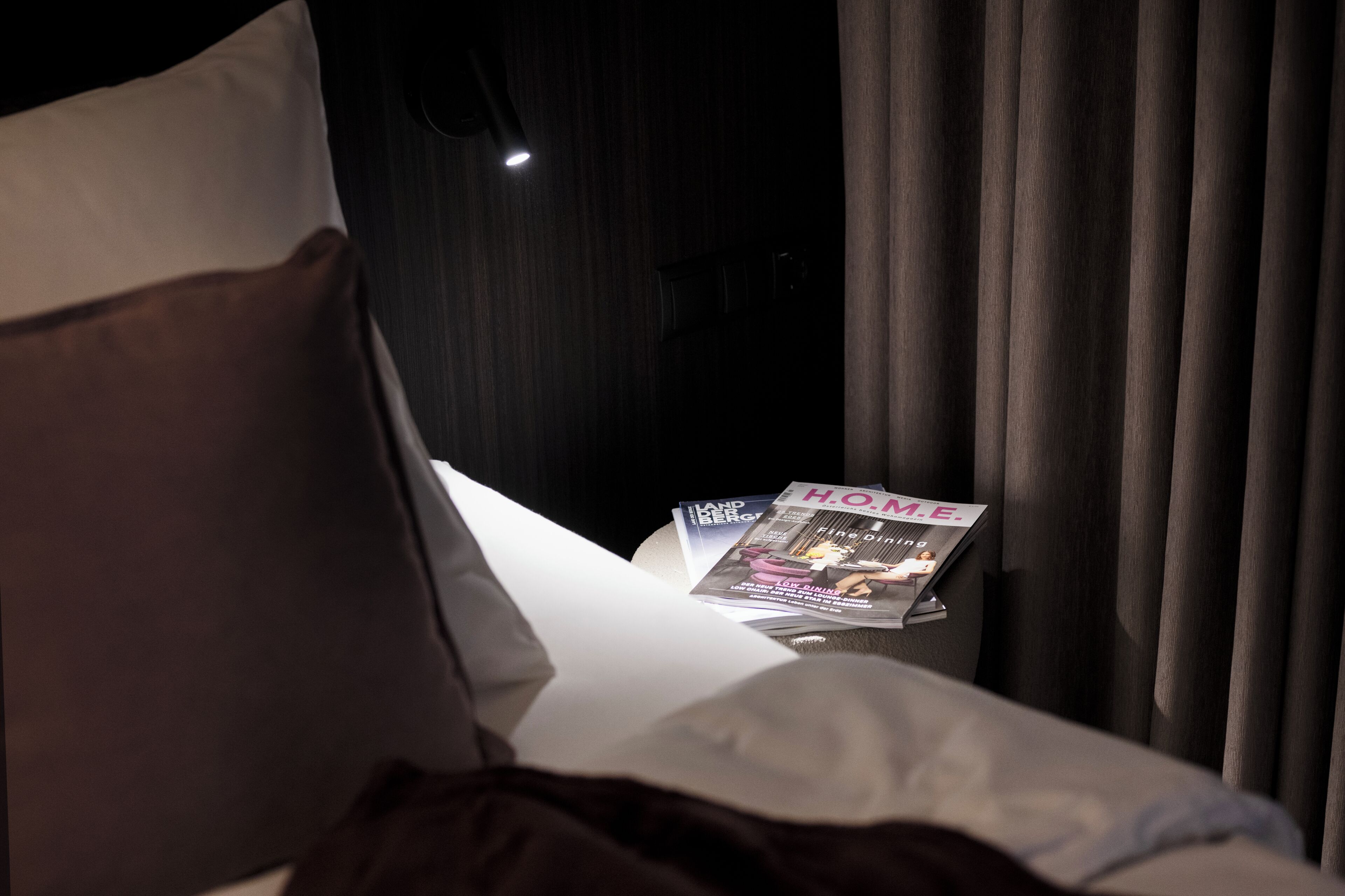 Una habitación de hotel con una cama, una revista sobre una mesita y una ventana con cortinas.