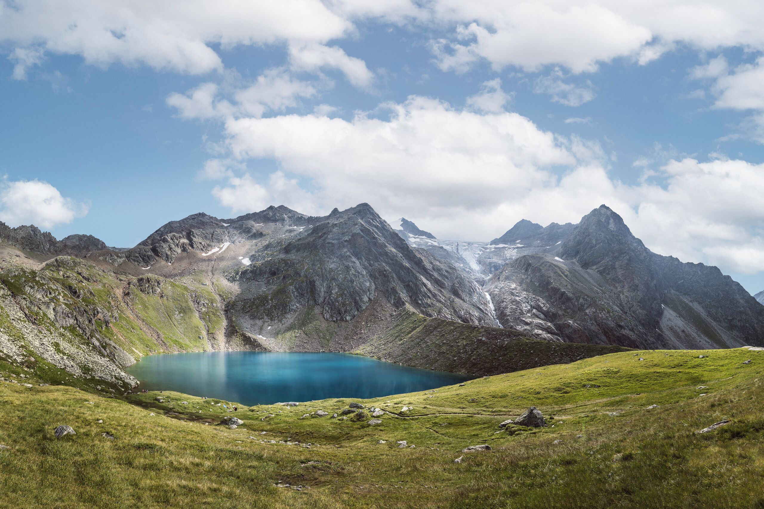 Un paysage montagneux avec un lac d’un bleu profond, entouré de reliefs rocheux et de prairies.