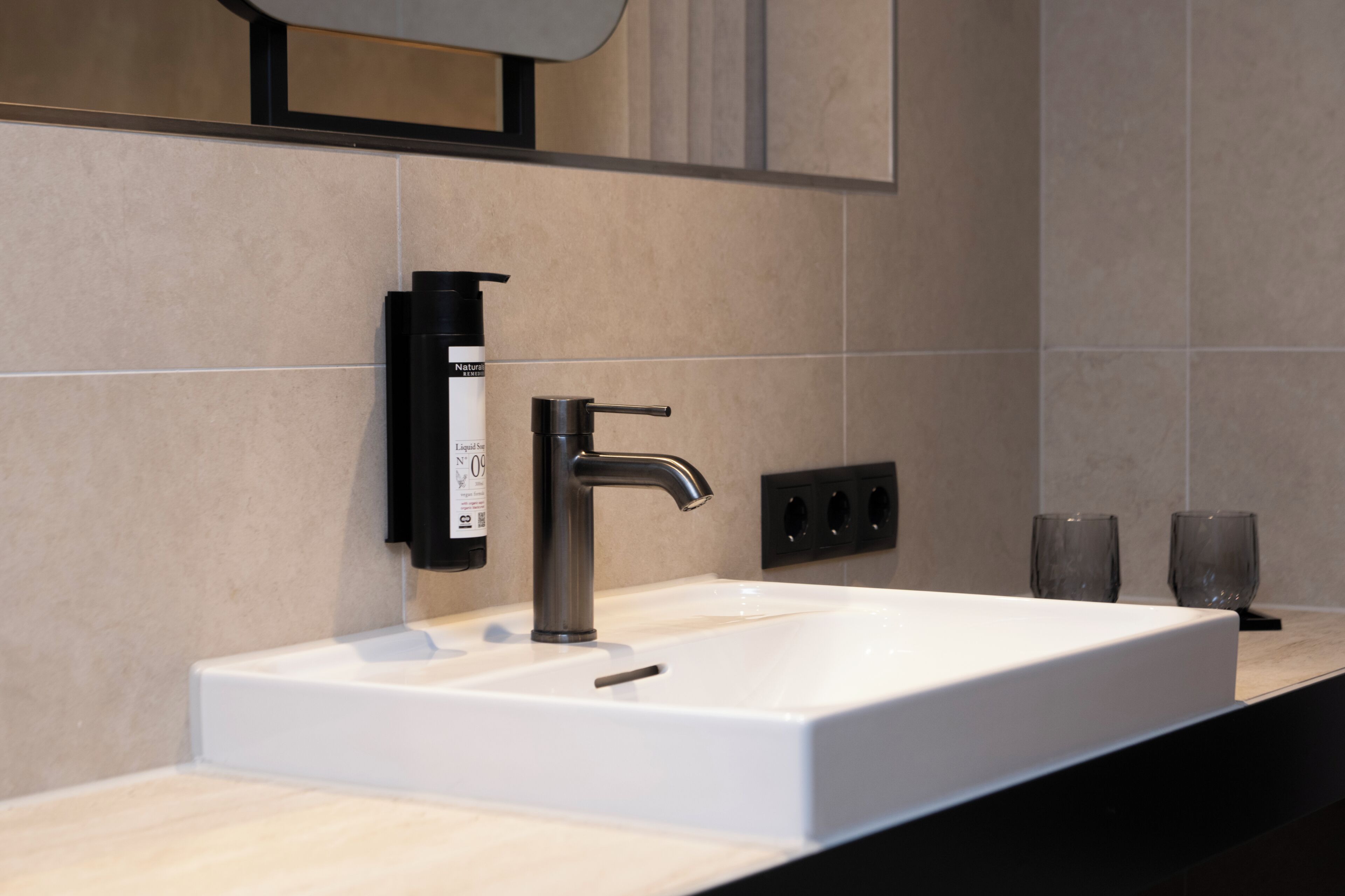 Une salle de bain moderne avec un lavabo blanc, un distributeur de savon noir et un miroir au-dessus.