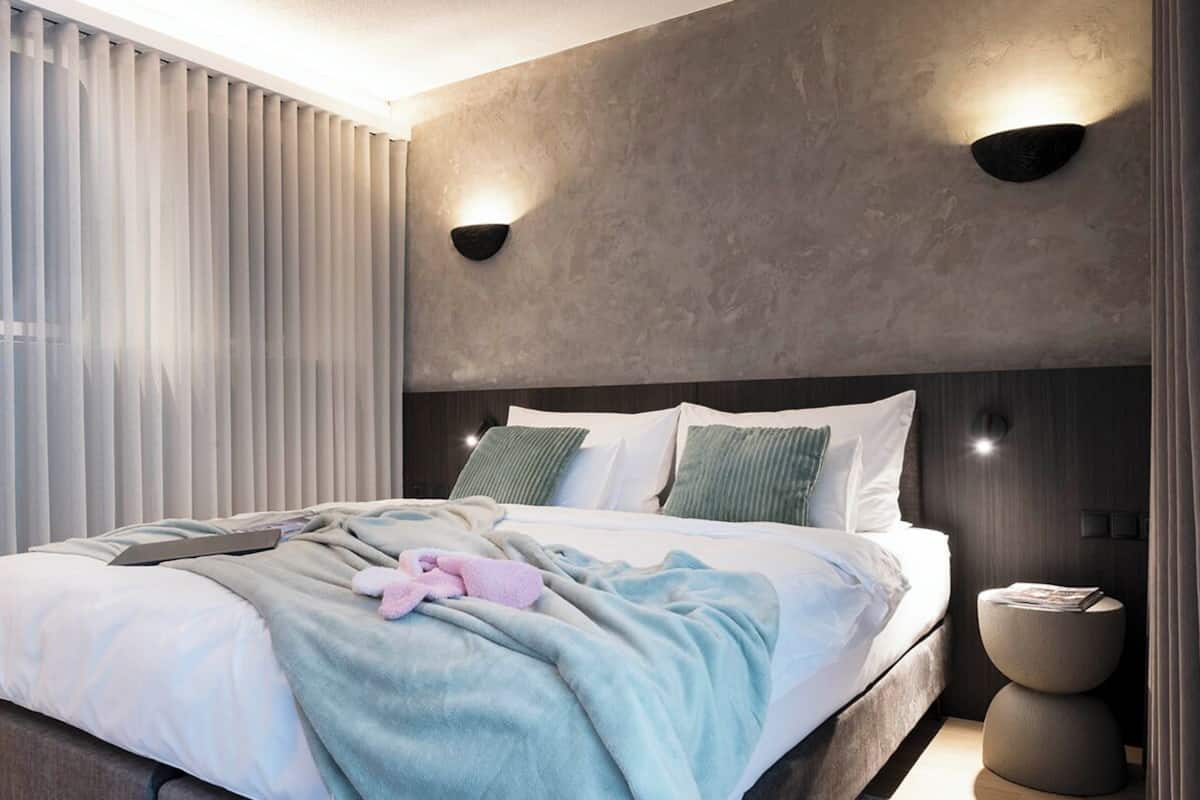 Un dormitorio moderno con una cama grande, dos luces fijadas en la pared y una mesita de noche con una revista.
