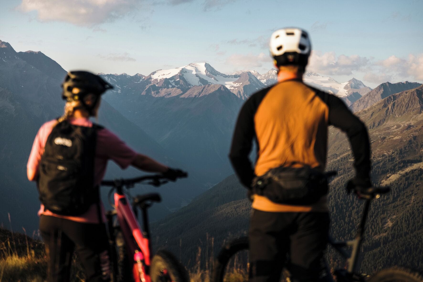 Two people on bicycles with a mountainous landscape in the background.