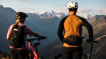 Two people on bicycles with a mountainous landscape in the background.