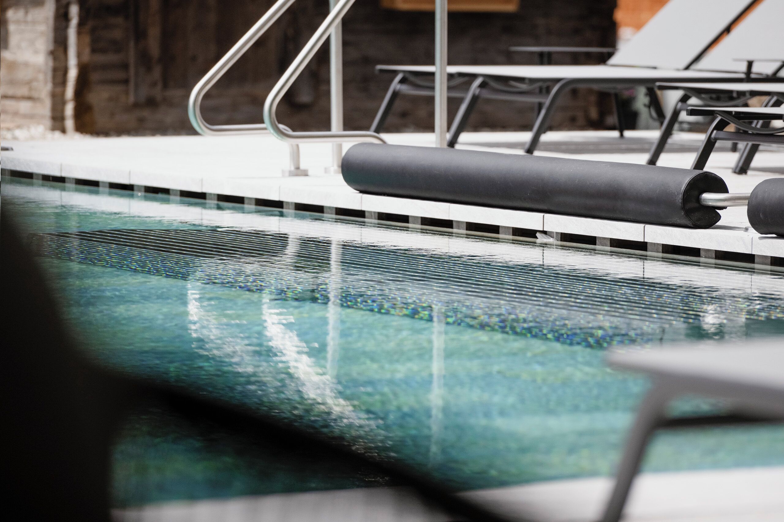 Ein Schwimmbecken mit klarem Wasser, einer gefliesten Kante und Metallgeländern.
