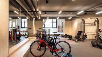A gym with a stationary bike, weightlifting equipment, and kettlebells.