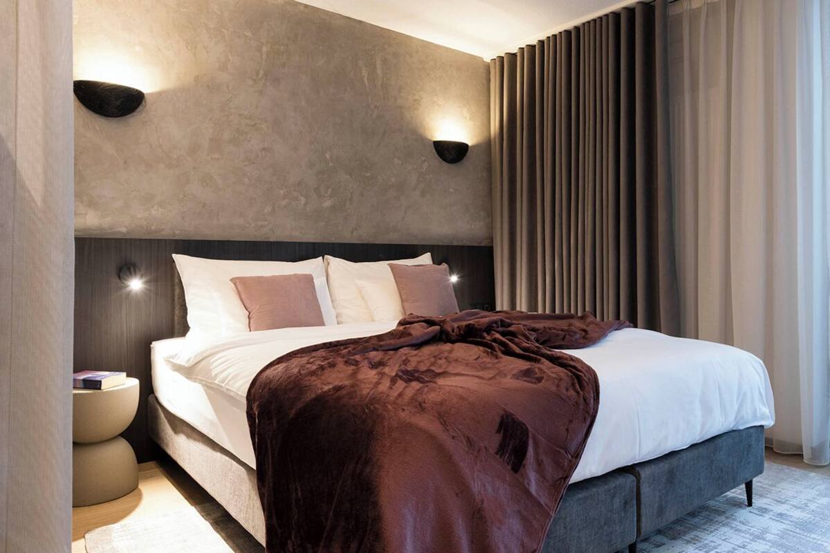 Un dormitorio moderno con una cama grande, dos lámparas de pared y un ventanal con cortinas.