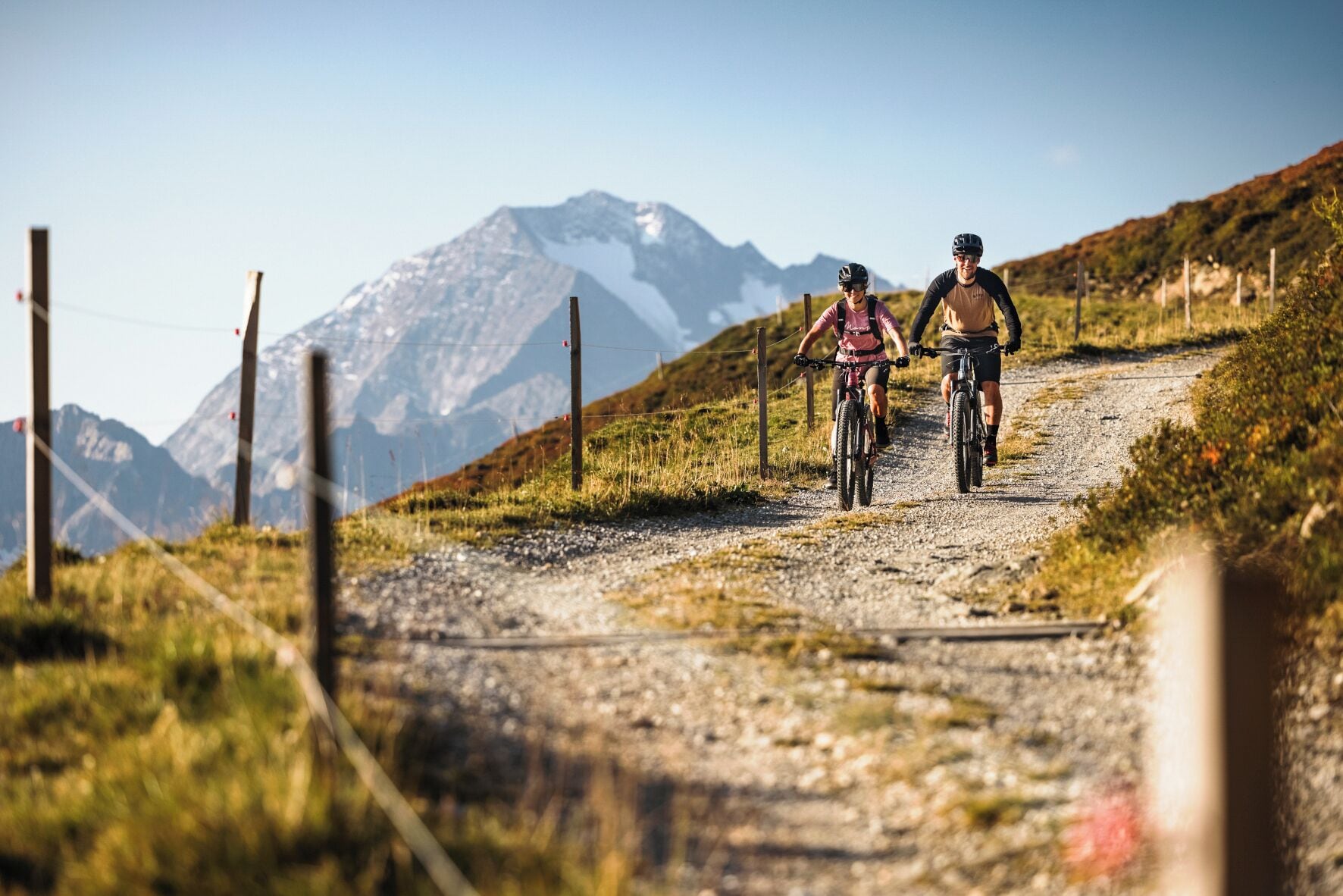Dos ciclistas en un camino de grava, con una montaña al fondo.