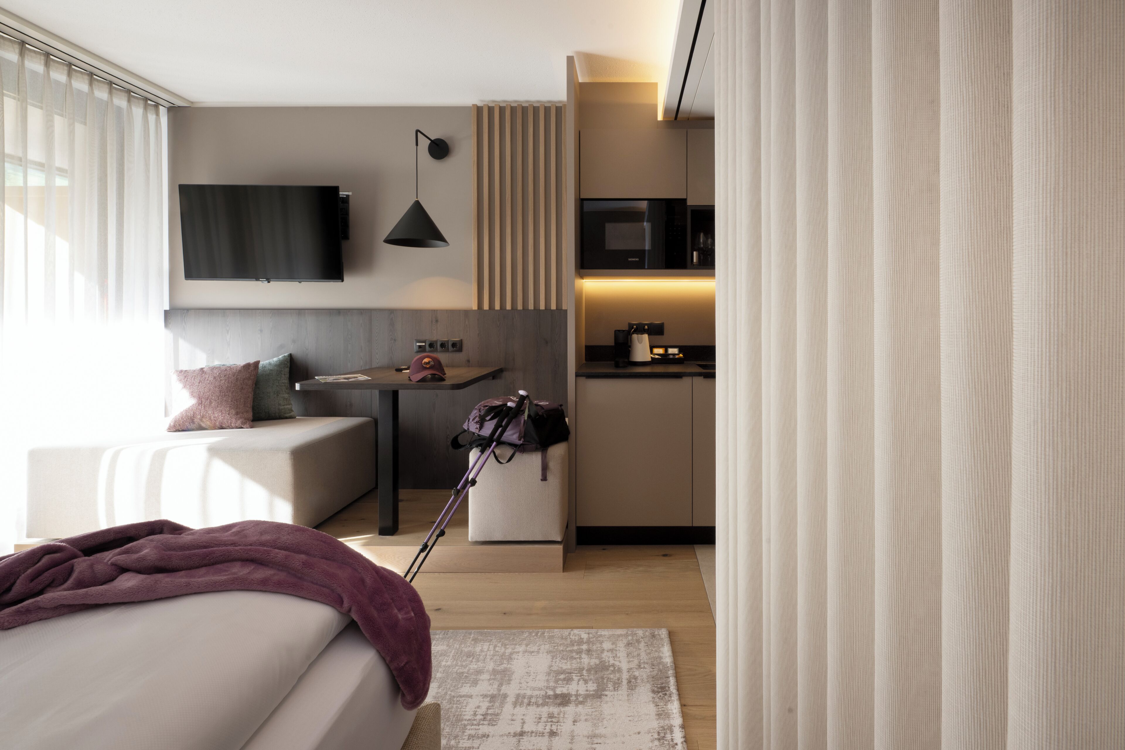 Una habitación de hotel moderna con una cama, un escritorio, una kitchenette y un televisor montado en la pared.
