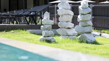 Een stenen cairn in een grasrijk gebied, met een zwembad en ligstoelen op de achtergrond.