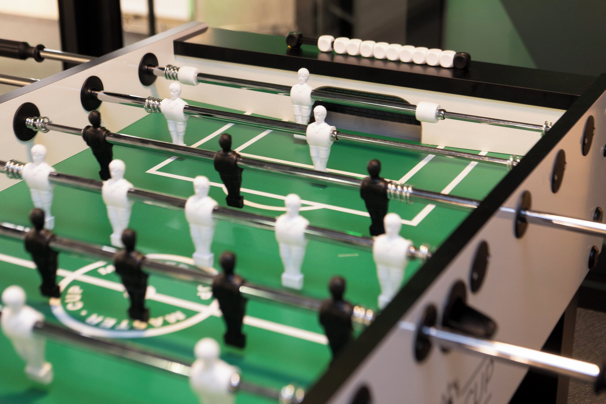 Gros plan d’un baby-foot avec deux équipes de joueurs miniatures, une équipe en noir et l’autre en blanc, sur un tapis de jeu vert.