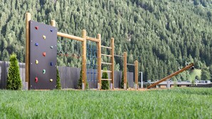 A playground with climbing and hanging equipment, surrounded by a grassy area and a forested hill in the background. - ELVA Premium Apartment Hotel (Neustift Im Stubaital)