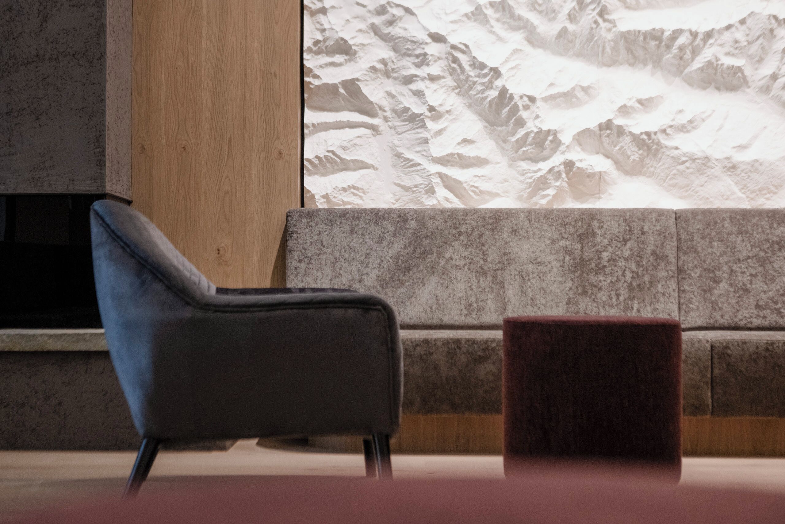 Una habitación moderna con un sillón azul oscuro, un reposapiés rojo y un amplio ventanal con vistas a la montaña.