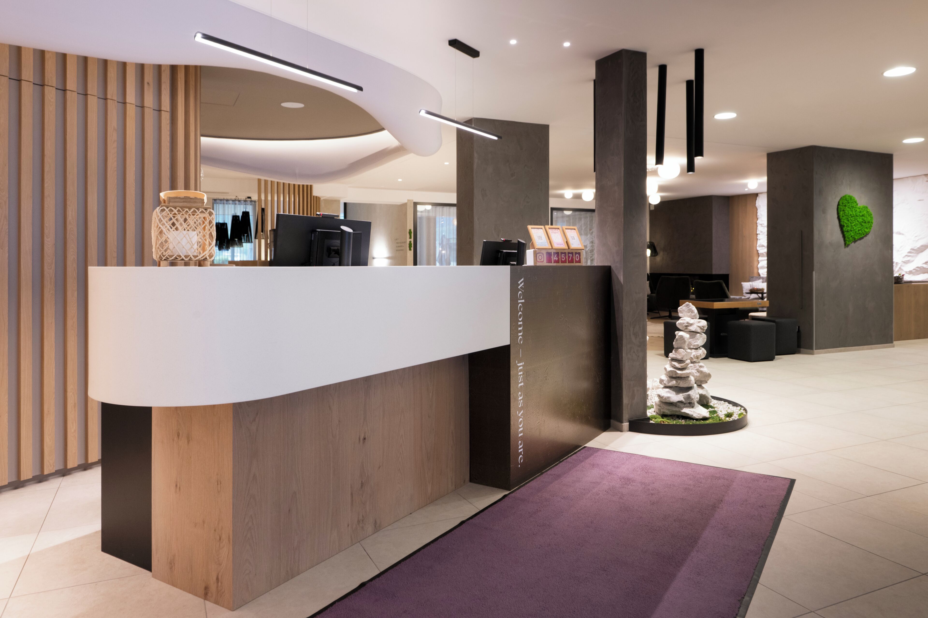 En modern receptionsdisk med träfinish, en digital skärm och ett receptionsområde med en grön hjärtformad dekoration på väggen.