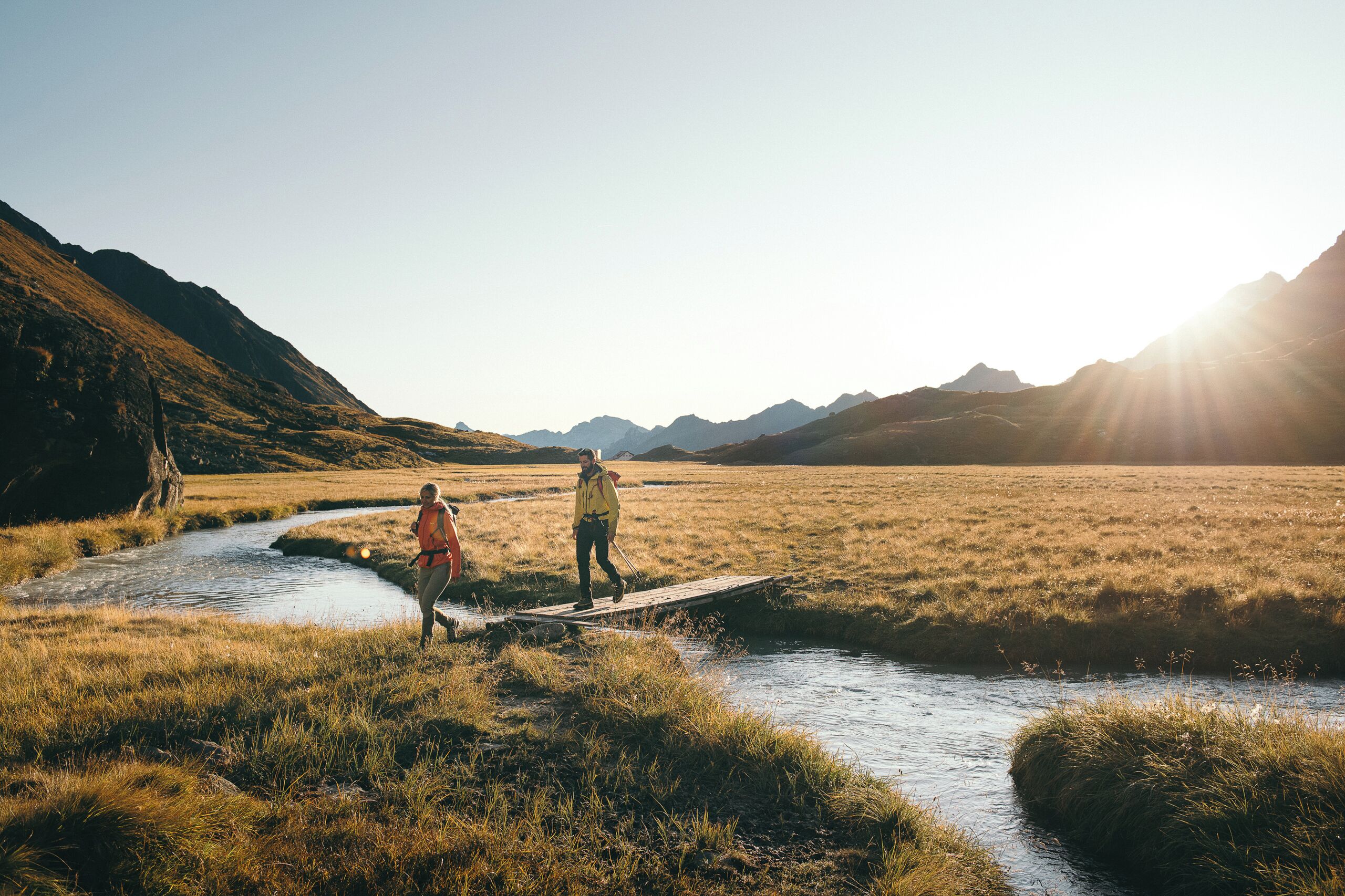 A river crossing with two people walking on a wooden bridge.