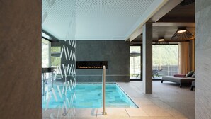 Un espace piscine intérieure moderne, doté d’une paroi en verre transparent, d’un panneau avec du texte et d’un coin salon offrant une vue sur l’extérieur.