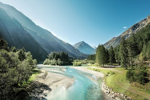 Un río serpentea a través de un paisaje montañoso con bosques frondosos y cielos despejados.