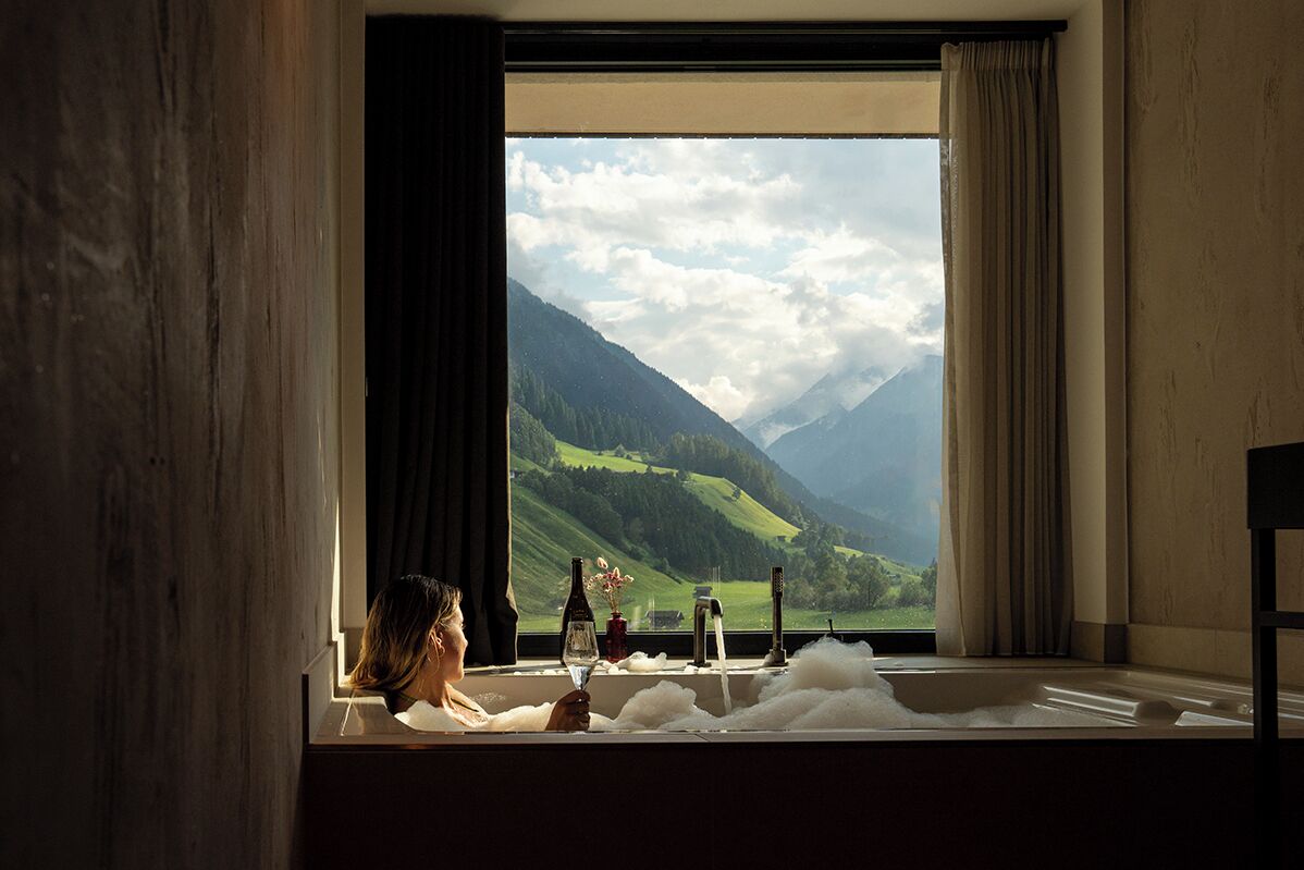 Una persona relajándose en una bañera con vista a montañas y un lago.