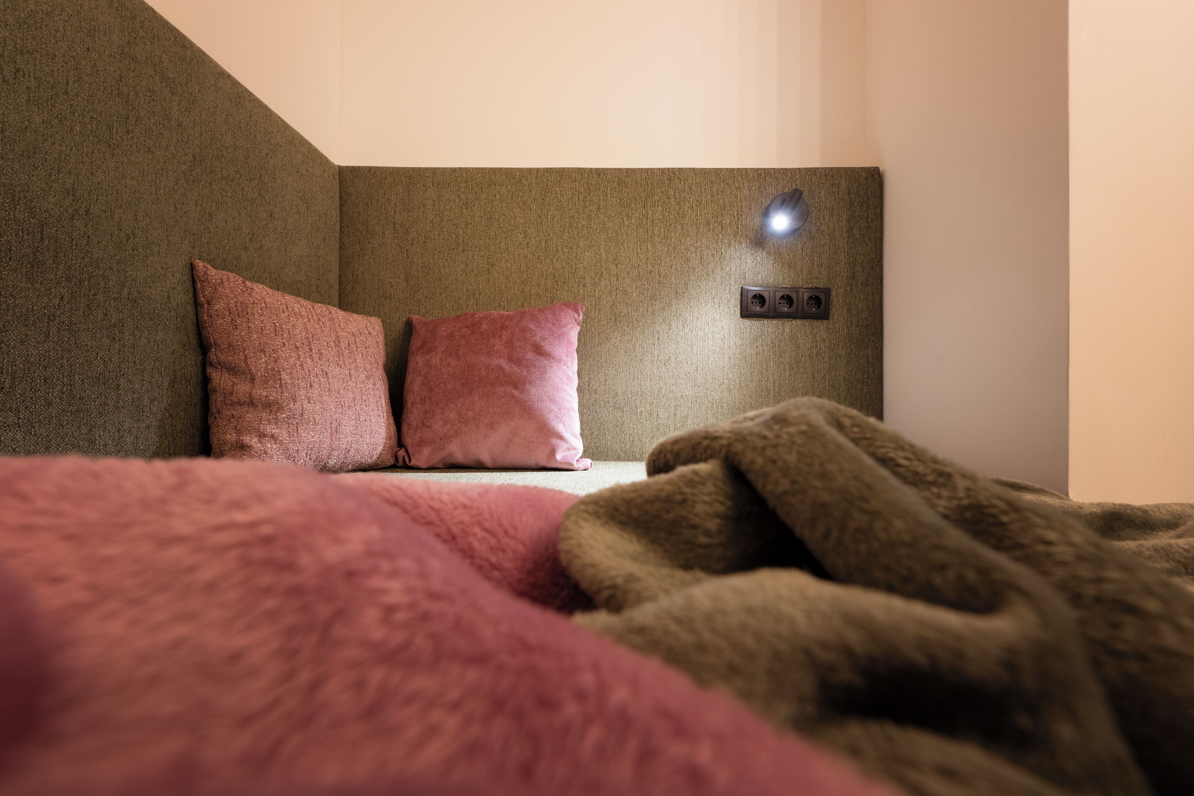 A bedroom with a bed, two pillows, a wall-mounted light, and a power outlet.