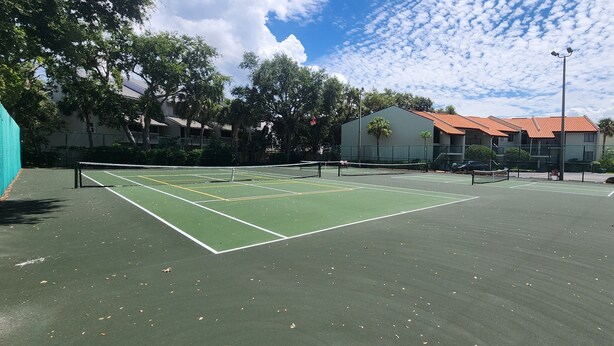 Ein Tennisplatz mit Netz, umgeben von Bäumen und Gebäuden.