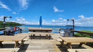 Eine Holzterrasse mit Picknicktischen und Grillplätzen mit Blick auf ein Gewässer.