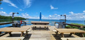 Eine Holzterrasse mit Picknicktischen und Grillplätzen mit Blick auf ein Gewässer.