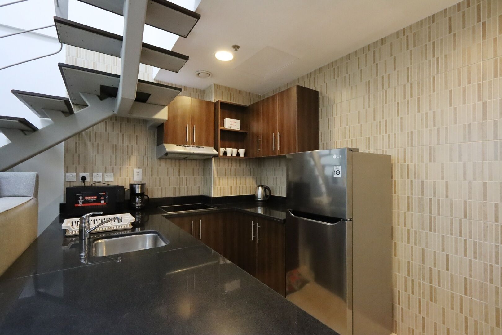 Una cocina moderna con un refrigerador de acero inoxidable, armarios de madera oscura, una encimera negra y una estufa integrada.
