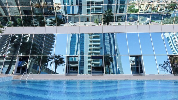 Un edificio moderno con fachada de vidrio reflectante, piscina y palmeras.