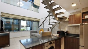 Una cocina moderna con lavadora integrada, un sofá gris y una escalera.