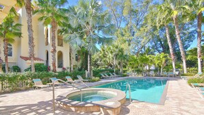 A pool area with lounge chairs, a hot tub, and palm trees. - La Casa AMI Beachside-Beachfront Condo w/ Heated Pool, Hot tub & Garage Parking (Holmes Beach)