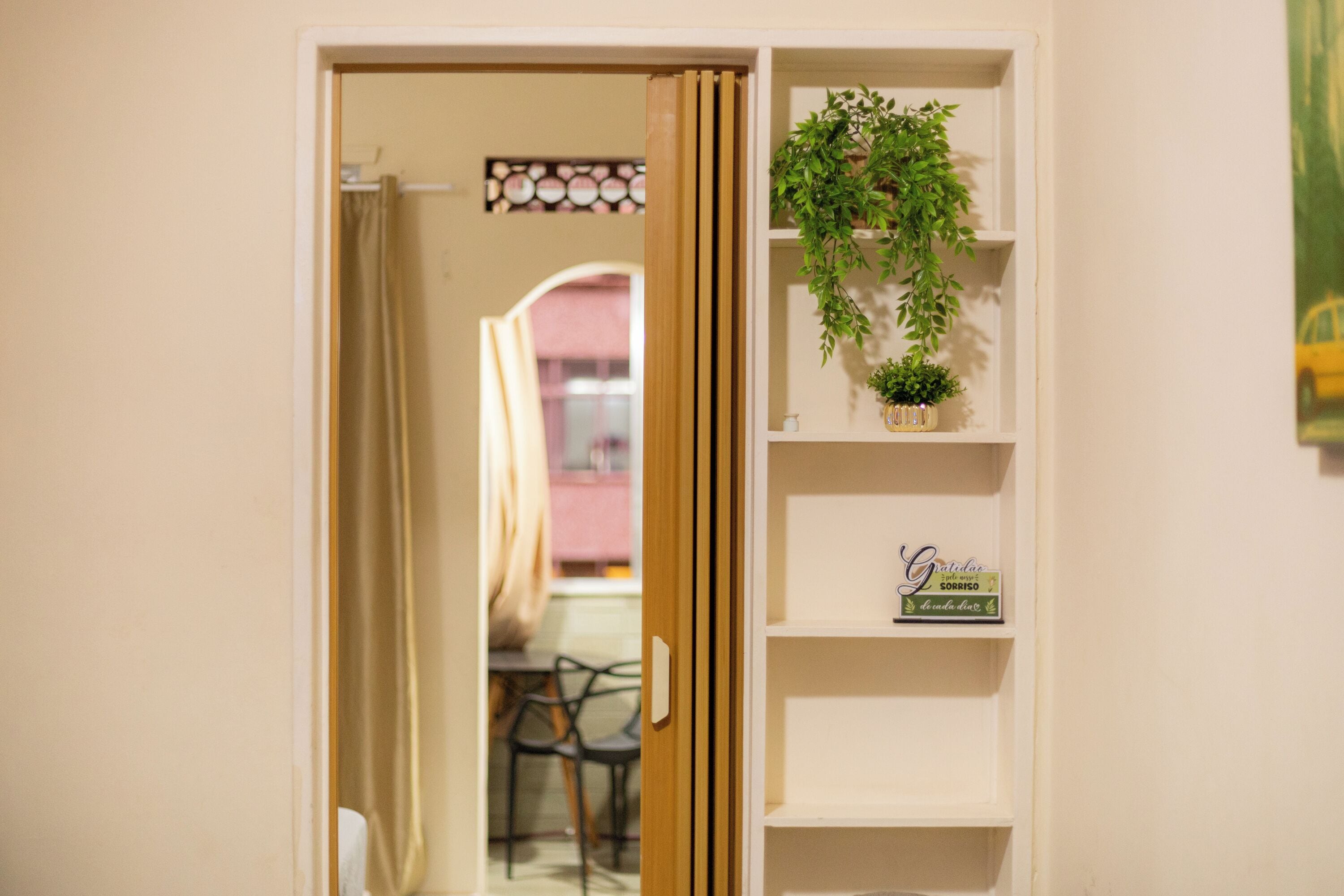A doorway leading to a room with a plant on a shelf, a small sign, and a glimpse of a dining area in the background.