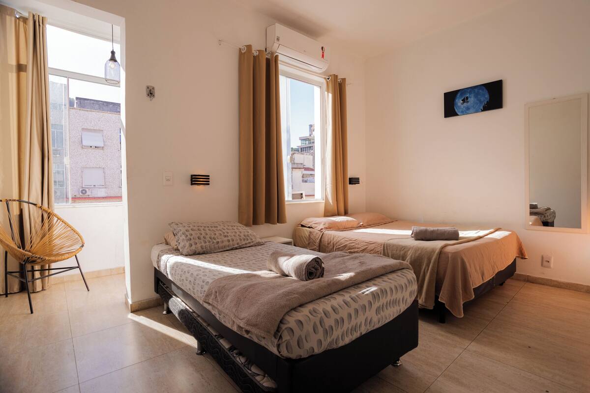 Un dormitorio con dos camas, una silla y un ventanal con cortinas.