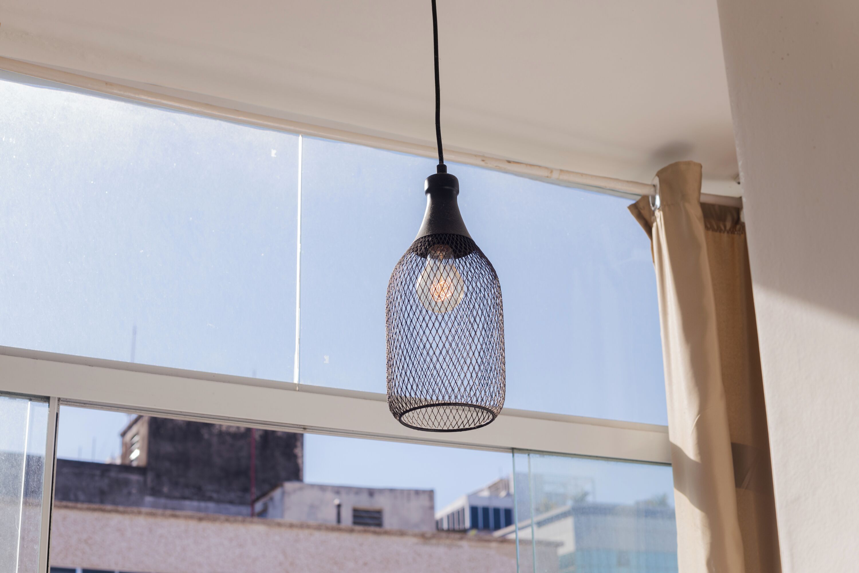 A hanging light fixture with a mesh design, suspended from a ceiling near a window.