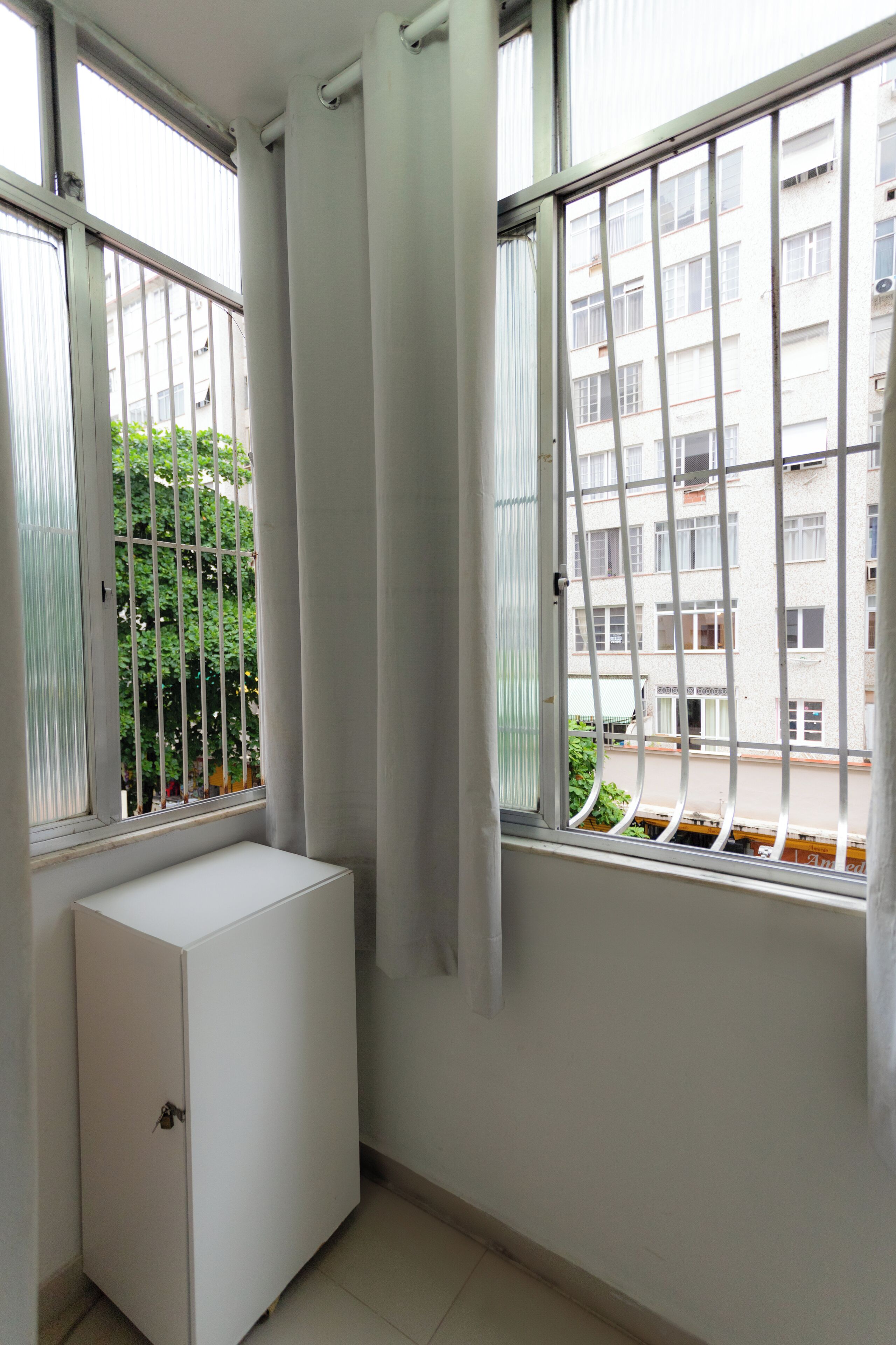 A room with a window, a white cabinet, and a view of a building with balconies.