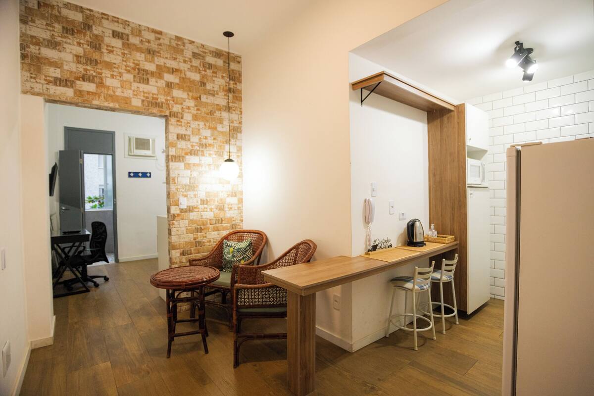 Una cocina compacta con una isla de madera, dos sillas de mimbre, una pequeña barra y un microondas.