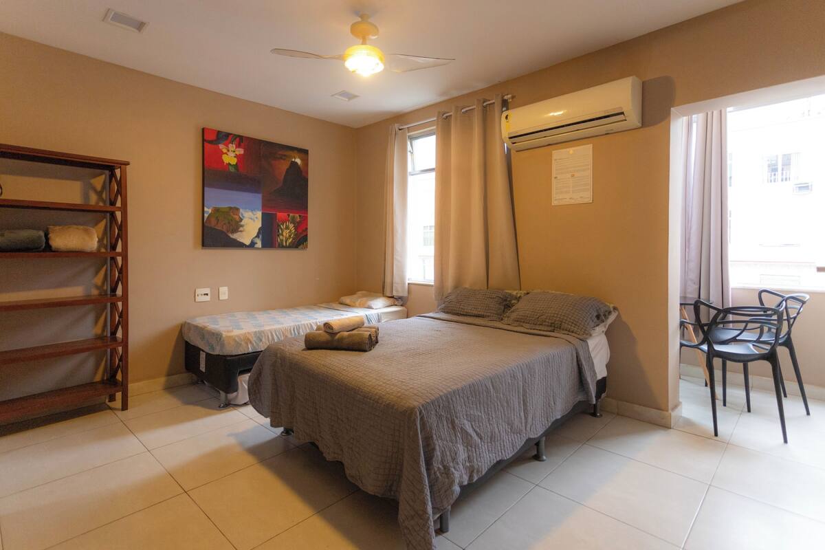 Un dormitorio con dos camas individuales, una estantería de madera, un ventilador de techo y una ventana con cortinas.