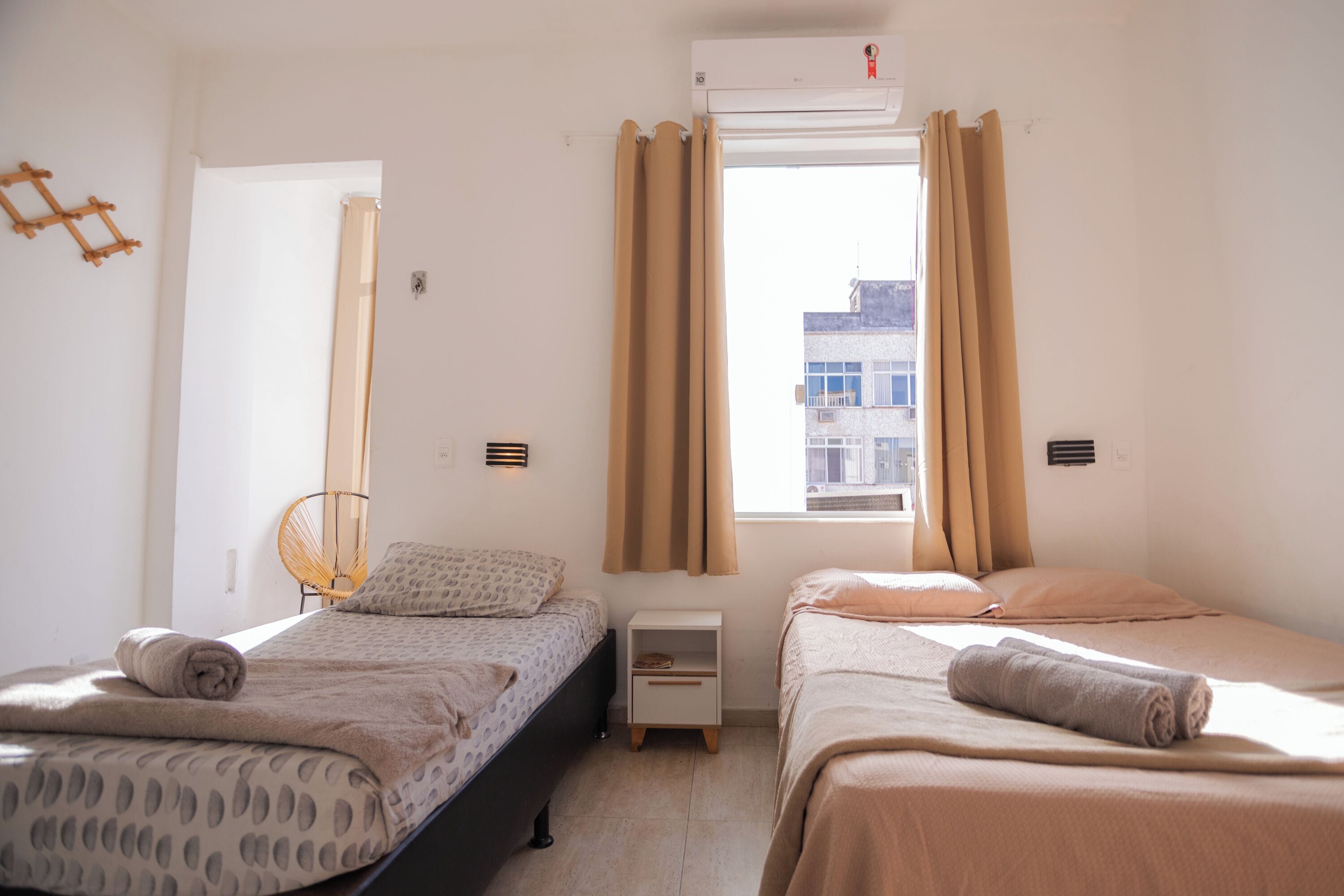 A room with two beds, a small bedside table, a chair, and a window with curtains.